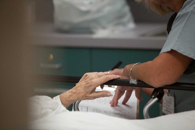 An older adult arranging family photos on a nightstand inside an assisted living apartment.