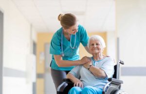 Staff member assisting an older adult with a walker in a bright communal living area.