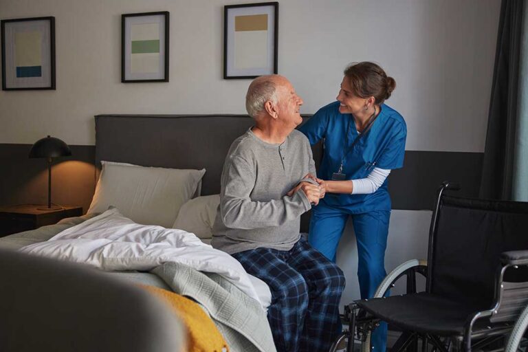 Older resident uses a tablet with a caregiver at a bright assisted living table.